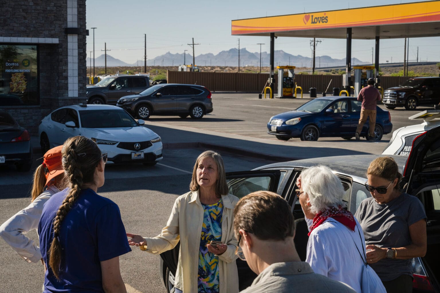 Volunteers with Battalion Search and Rescue gather in the parking lot of a Love’s truck stop in Santa Teresa, New Mexico, on April 26, 2025. The group prepares for a desert search as cars, gas pumps, and the Organ Mountains are visible in the background.