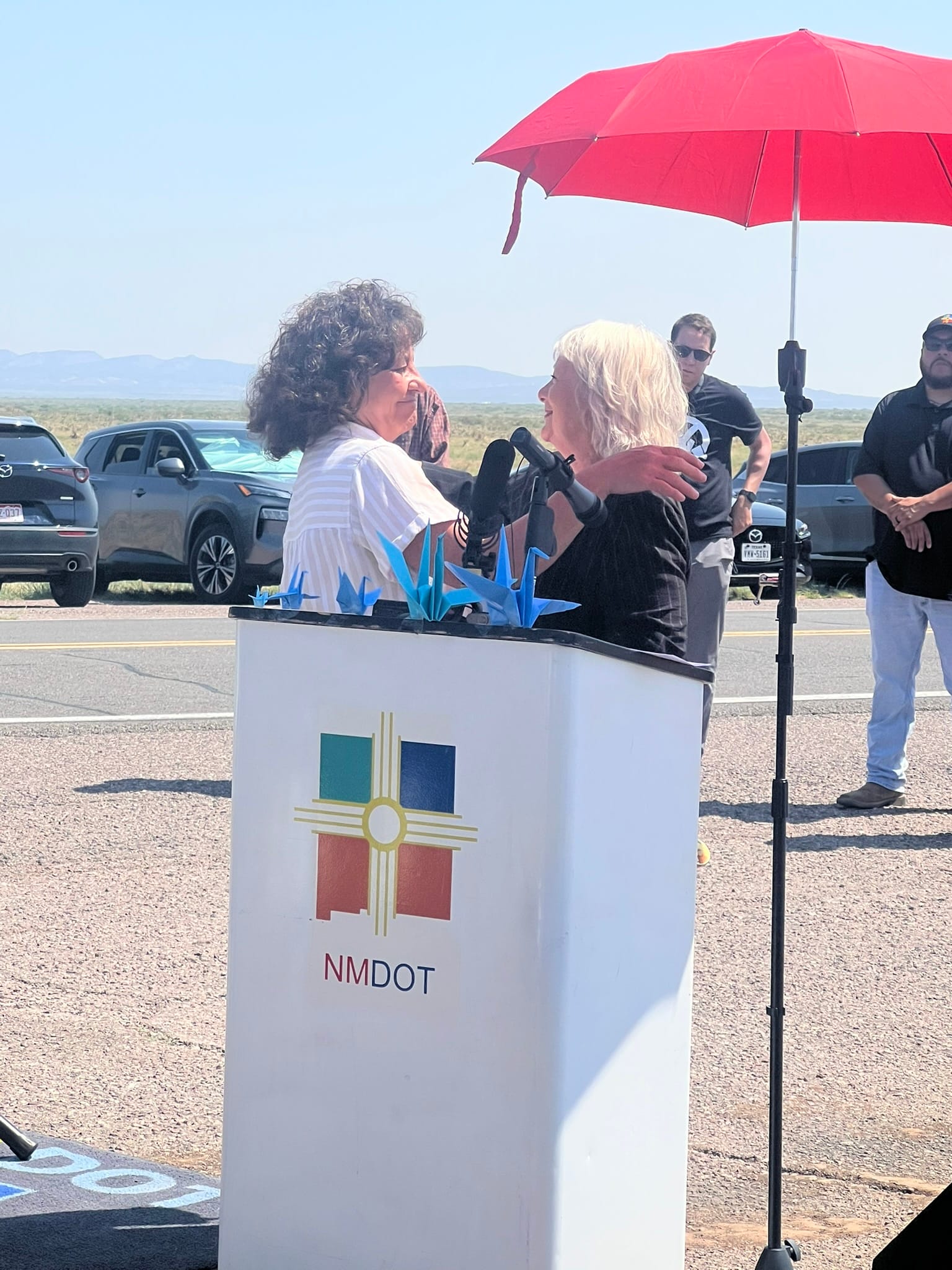 Tina Cordova embraces state Rep. Joanne Ferrary during a July 16, 2025, sign unveiling honoring nuclear testing downwinders and celebrating the expanded RECA law.
