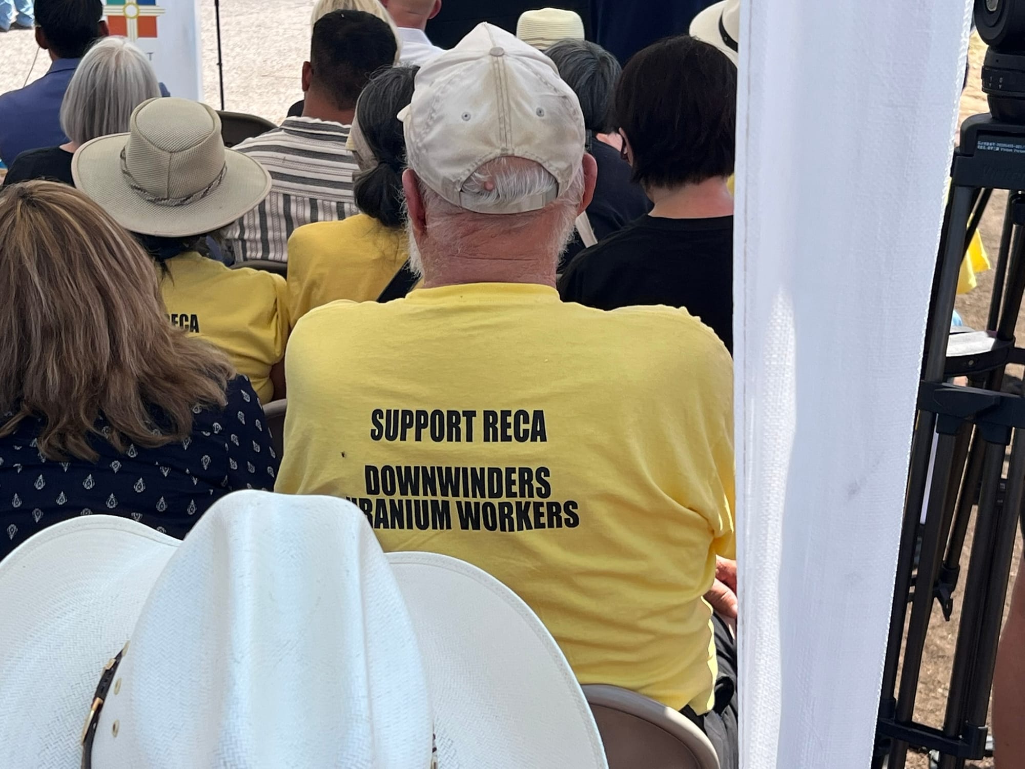 An attendee wears a yellow shirt reading 'Support RECA Downwinders Uranium Workers' during a July 16, 2025, sign unveiling honoring nuclear testing downwinders.