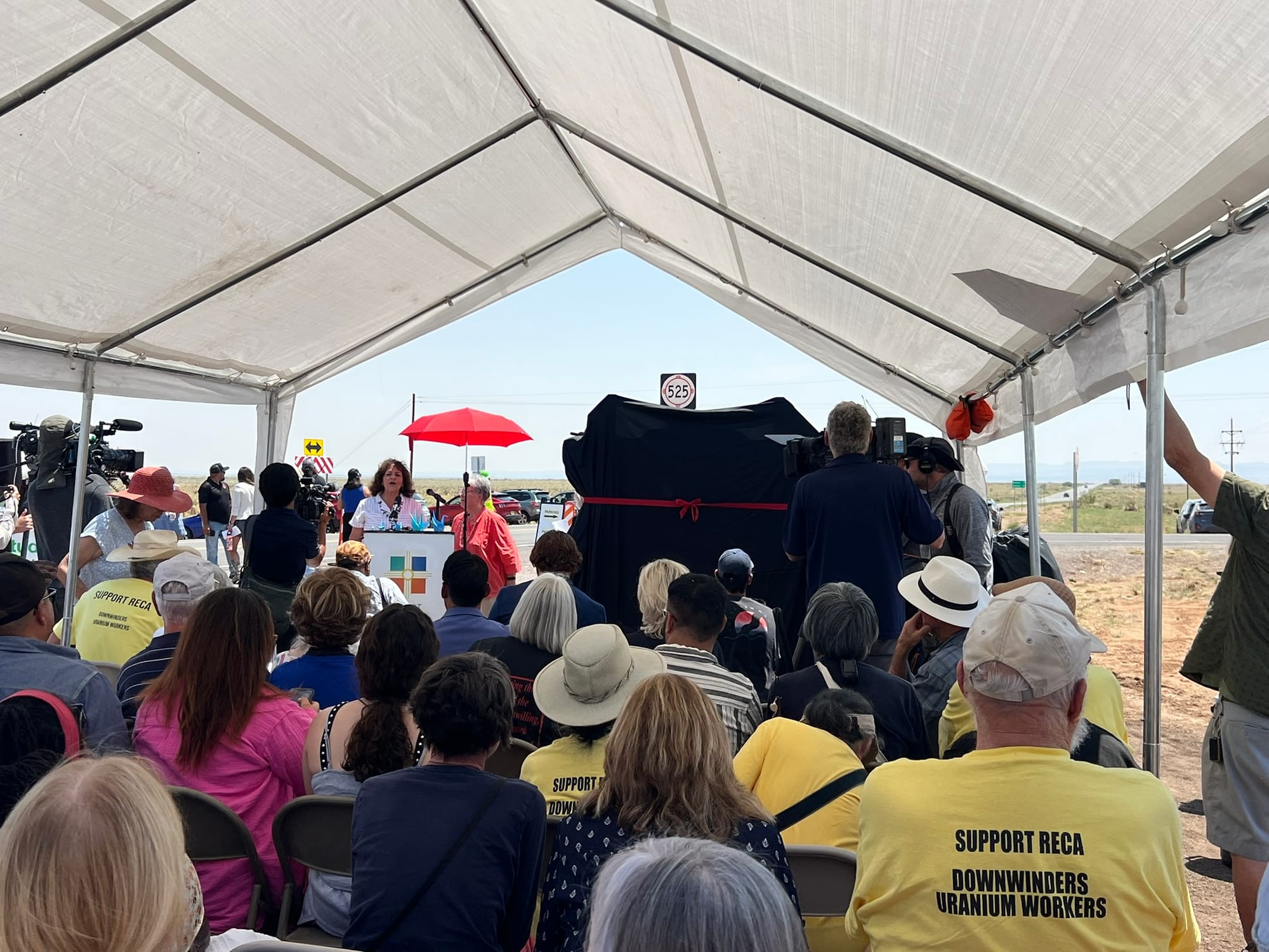 Tina Cordova speaks at a RECA celebration near Trinity Site as attendees in yellow ‘Support RECA’ shirts listen.