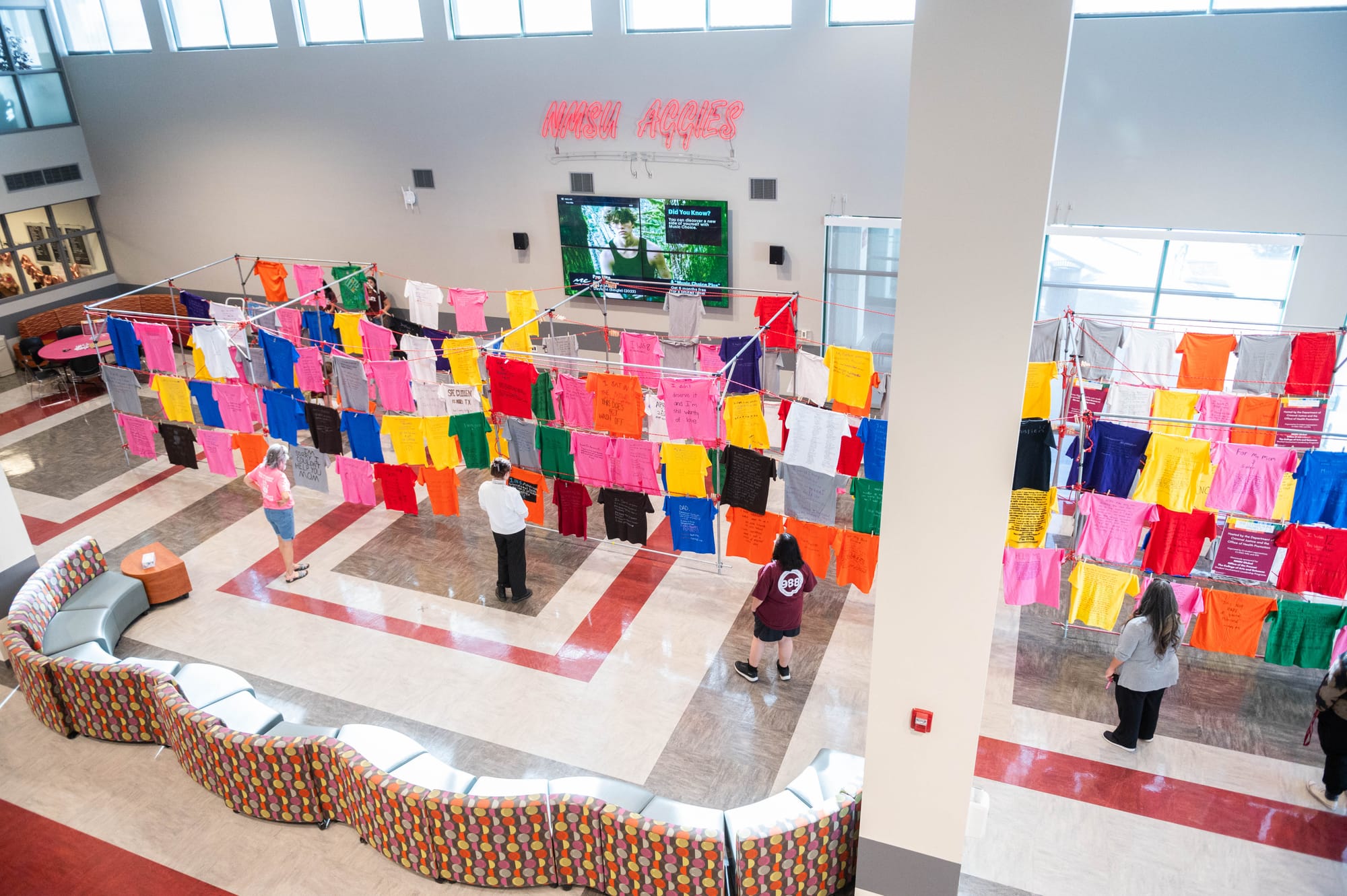 A wide view of NMSU’s Clothesline Project exhibit shows rows of colorful shirts hanging in Corbett Center, each displaying messages from survivors of violence and abuse.