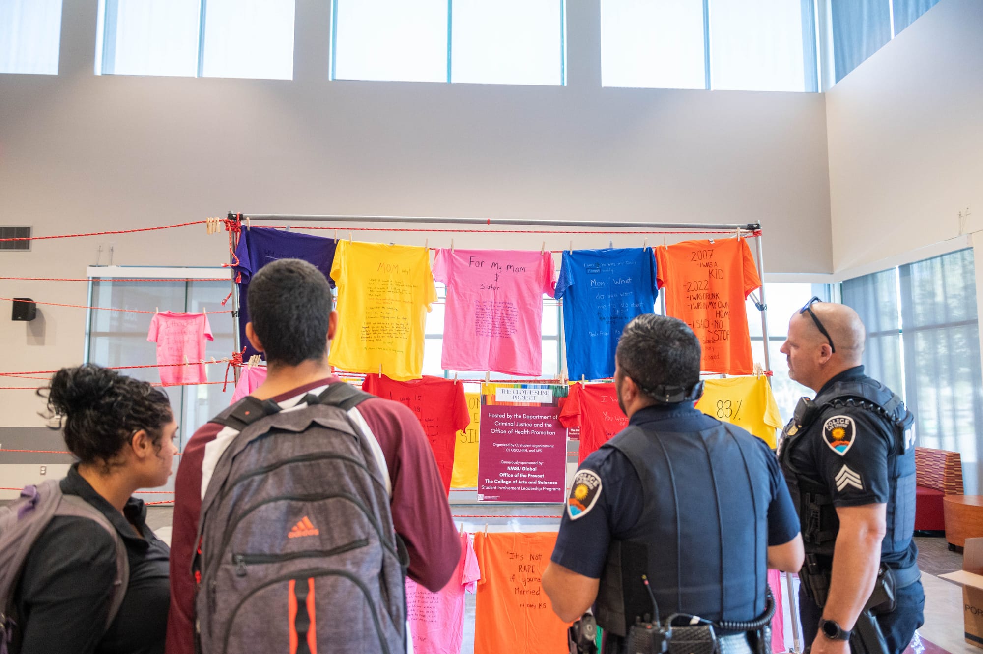 Two NMSU students and two Las Cruces police officers stand together reading T-shirts with survivor messages at a past Clothesline Project exhibit inside Corbett Center.