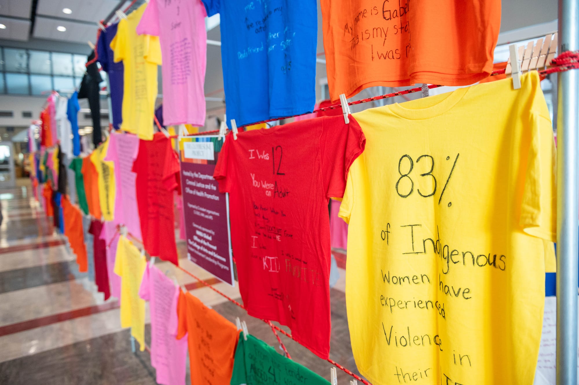 Rows of brightly colored T-shirts hang on display inside NMSU’s Corbett Center, each featuring handwritten messages and statistics about violence and survival.