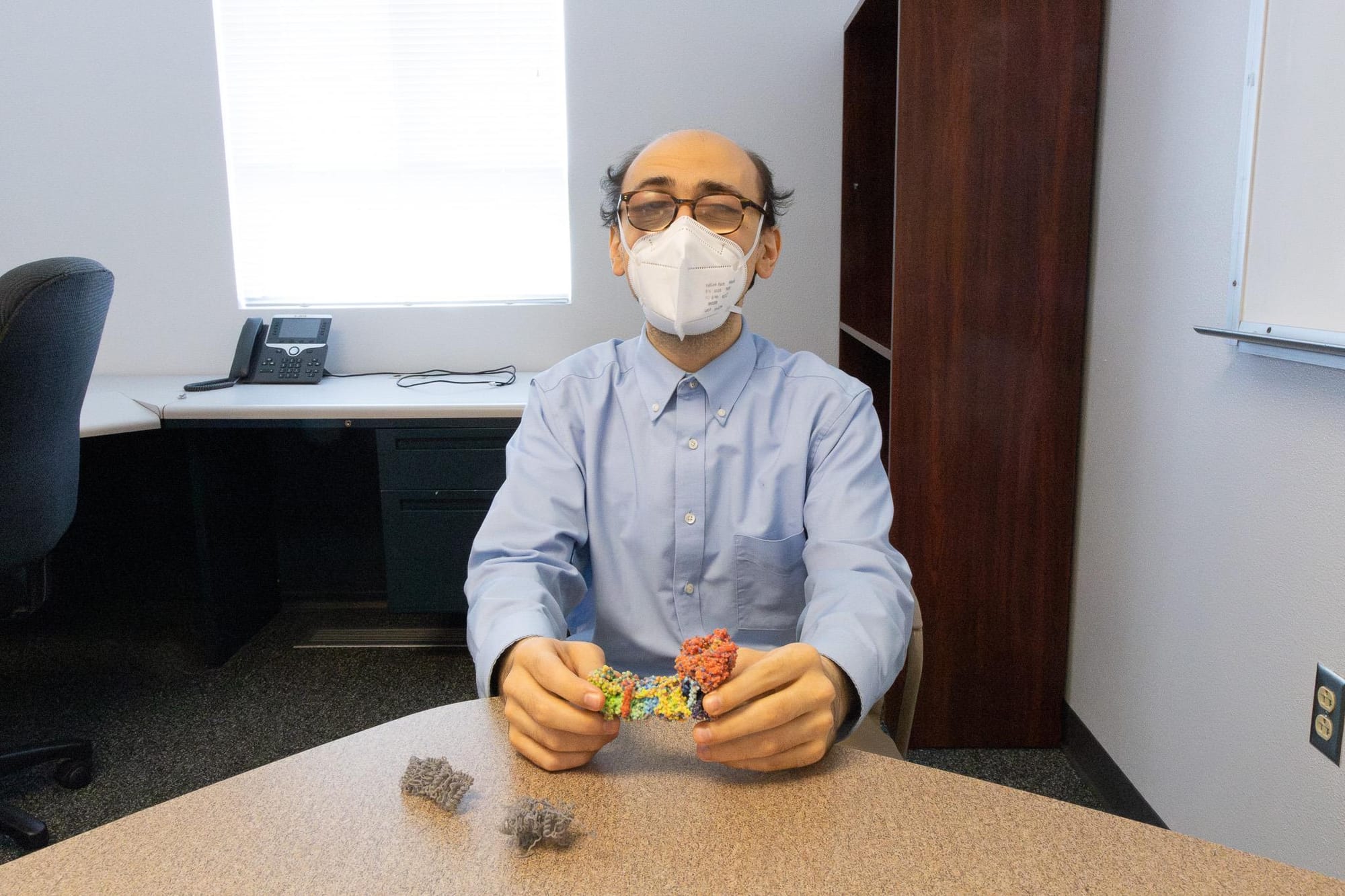 Guberman-Pfeffer sits at a table holding a colorful 3D molecular model, demonstrating tactile tools developed to help visually impaired scientists study chemistry and biology.