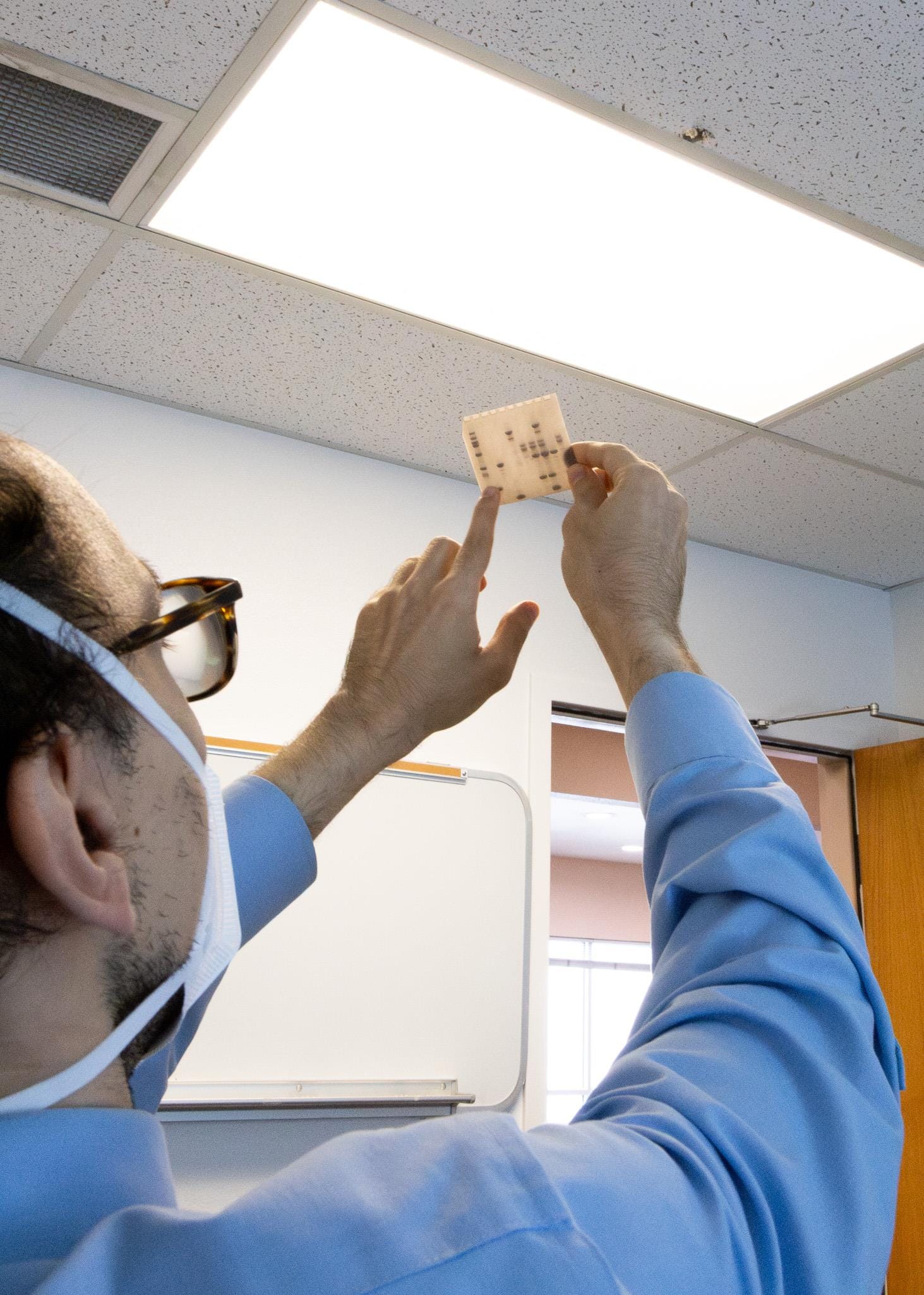 Matthew Guberman-Pfeffer, assistant professor at New Mexico State University, holds a translucent tactile sheet toward a light, showing raised patterns used to help students with visual impairments study molecular science.