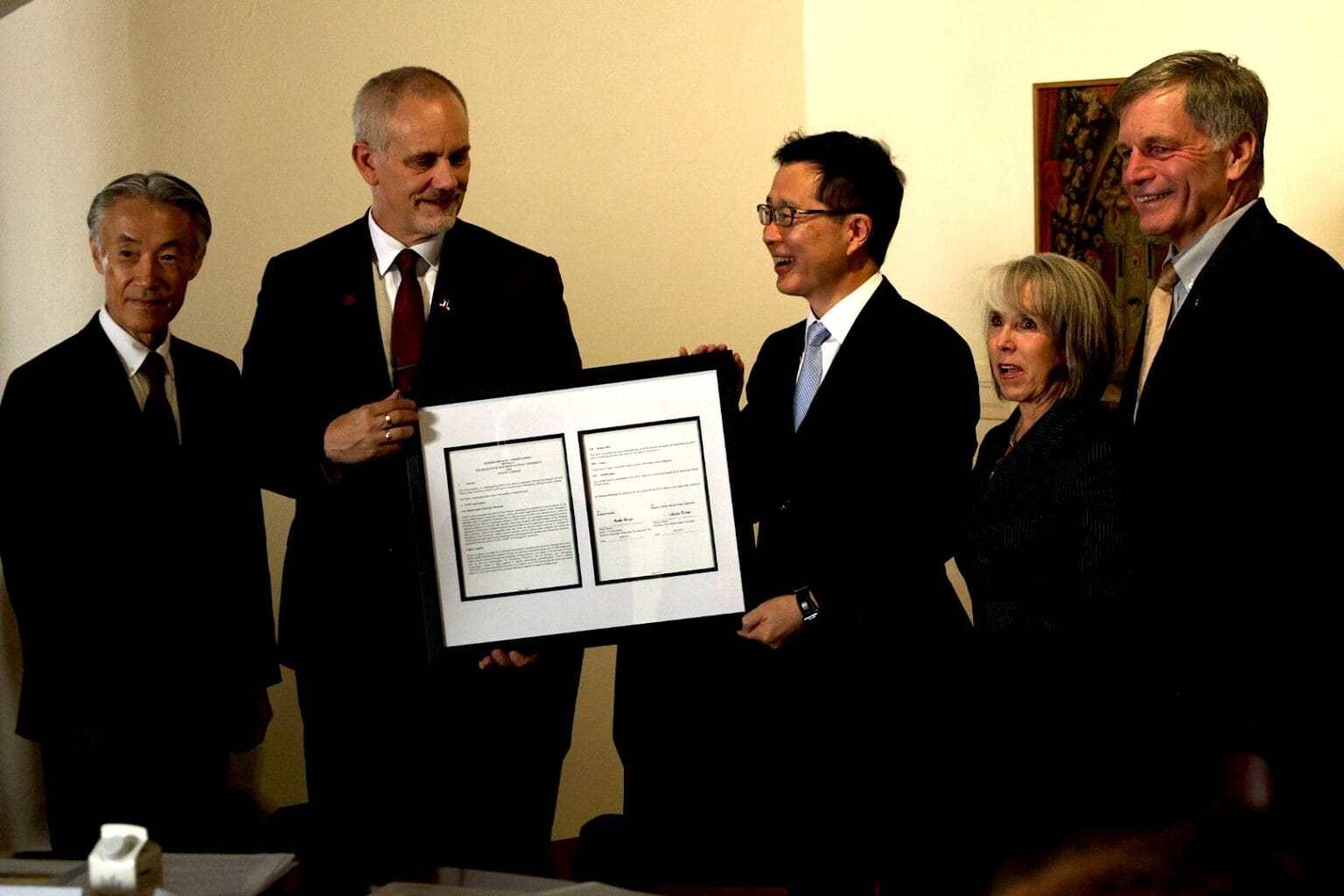 Five people stand together holding a framed document during a signing ceremony marking a new partnership between New Mexico State University and a Japanese technology company.