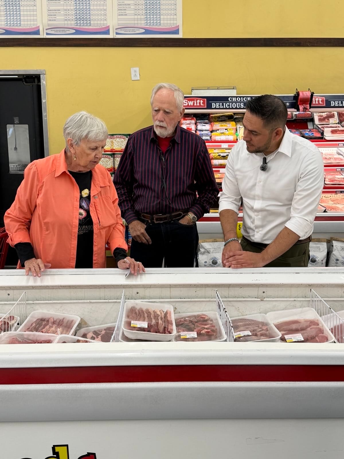 U.S. Rep. Gabe Vasquez stands with Las Cruces residents Karen and Jack Zilbert beside a freezer filled with packaged meat, discussing grocery prices during a visit to a local store.