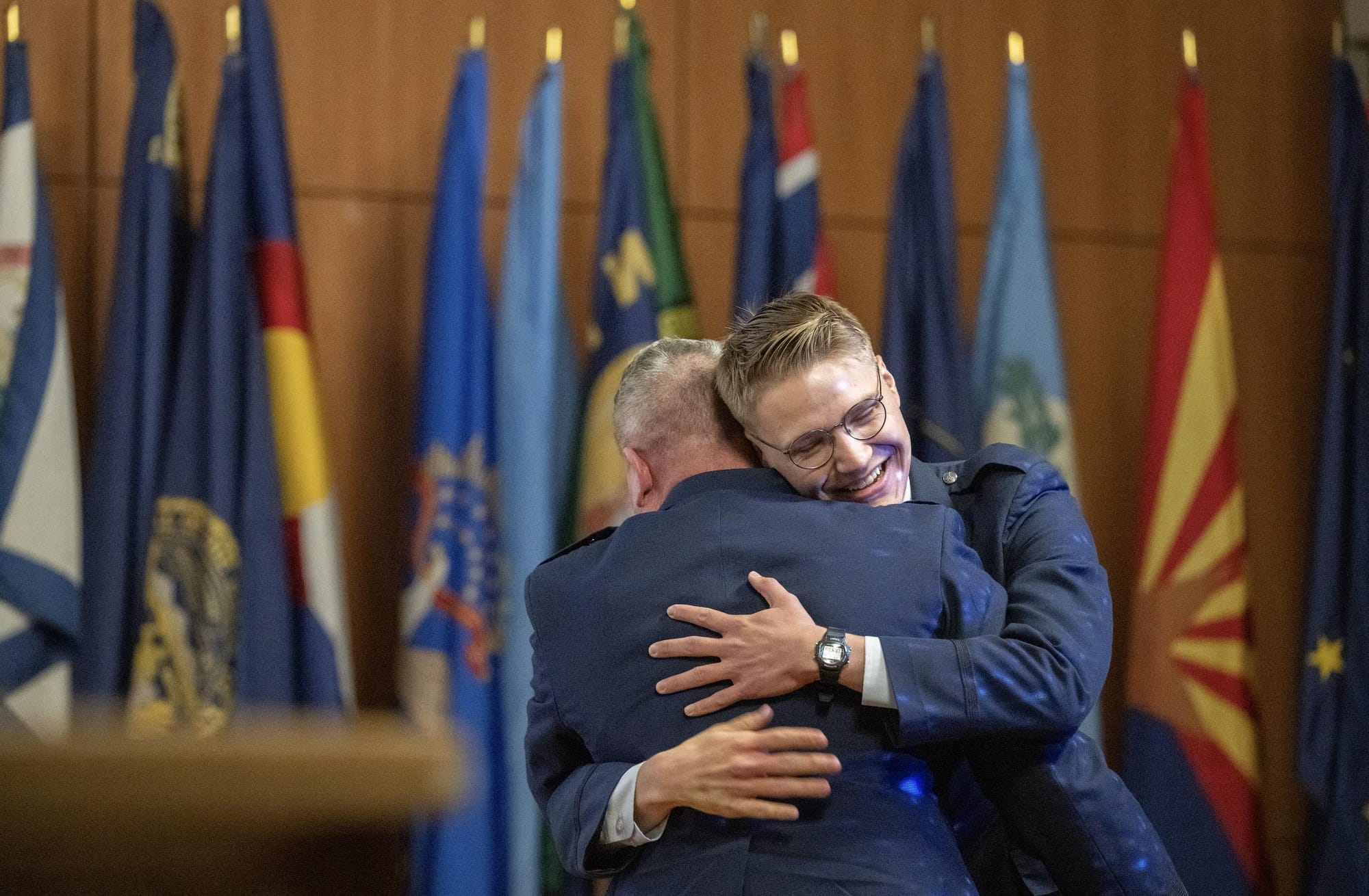 U.S. Air Force Brig. Gen. Lance French embraces his son following the son’s commissioning ceremony into the U.S. Space Force, with service flags displayed behind them.