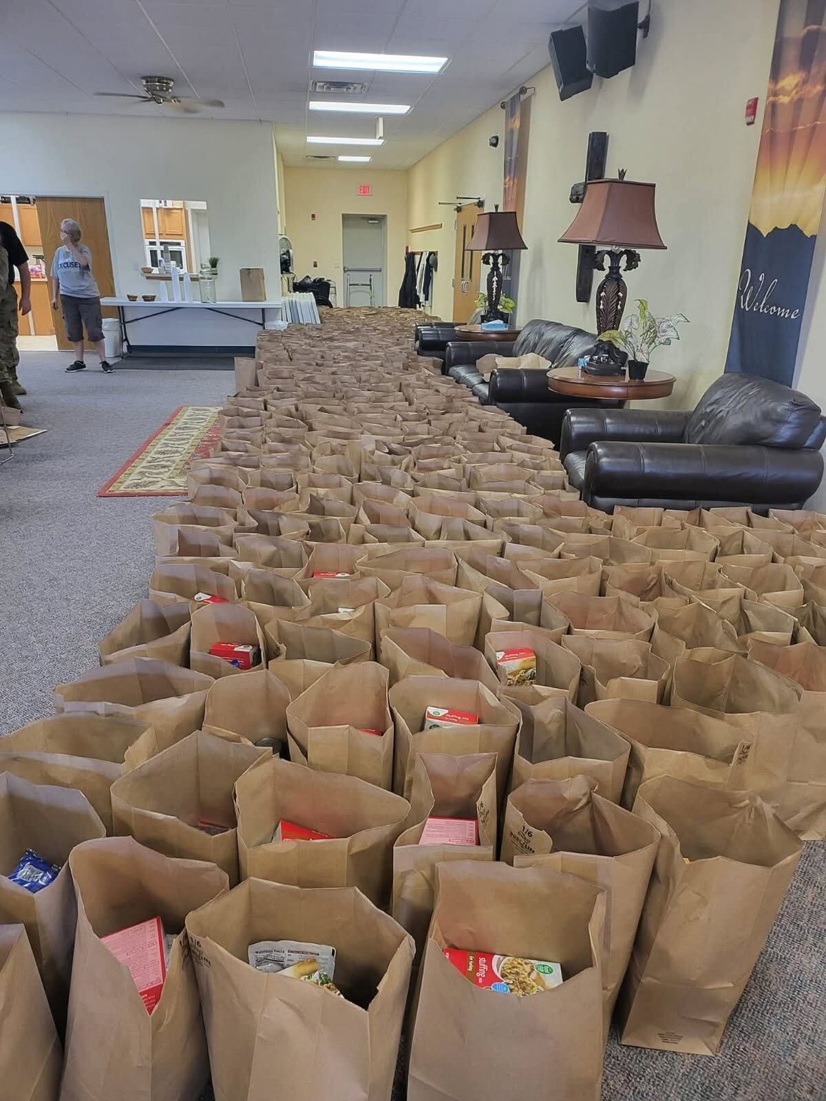 Rows of paper grocery bags filled with food line the floor of Shepherd's Closet, with volunteers working in the background.