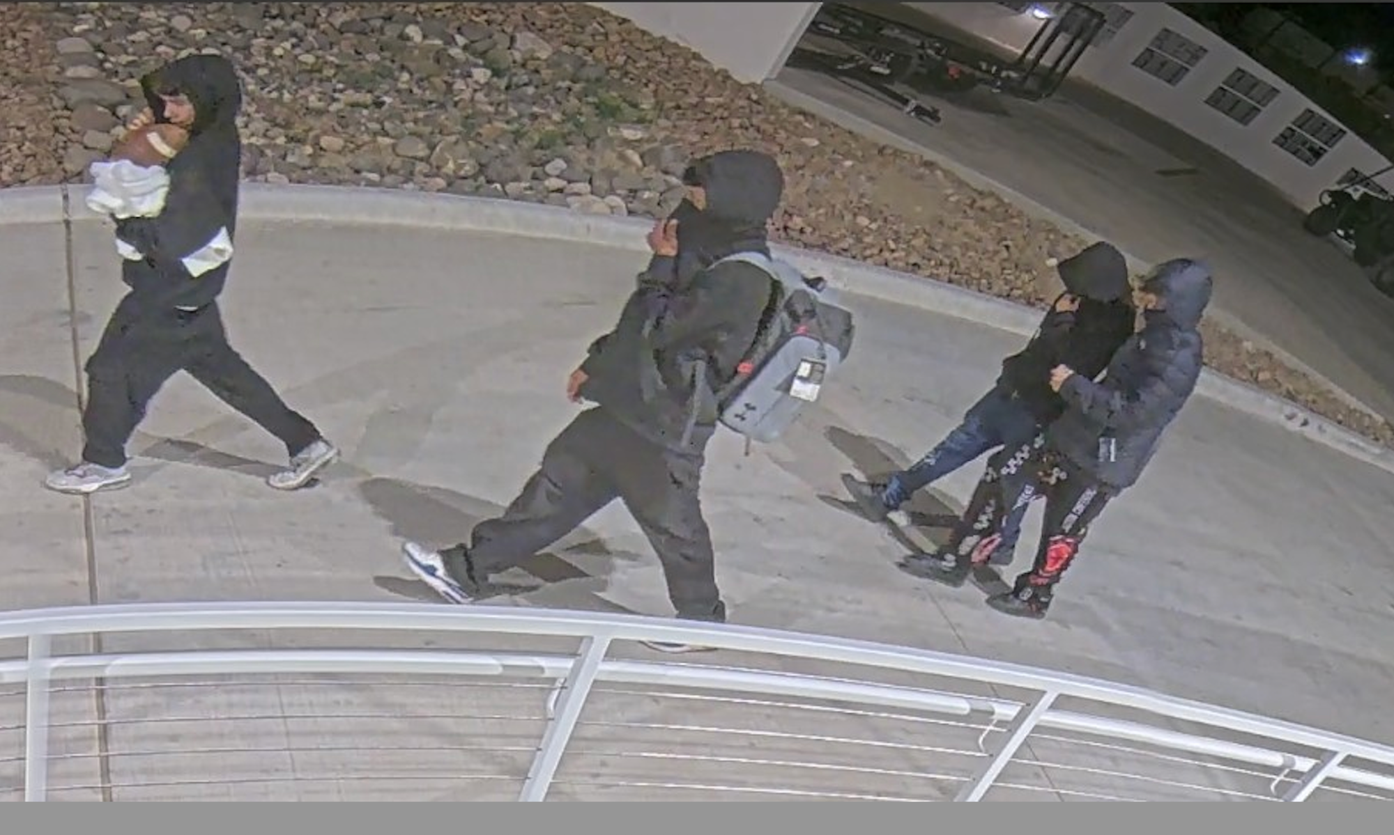 Surveillance image shows several individuals walking outside campus buildings during a burglary and vandalism investigation at New Mexico State University.