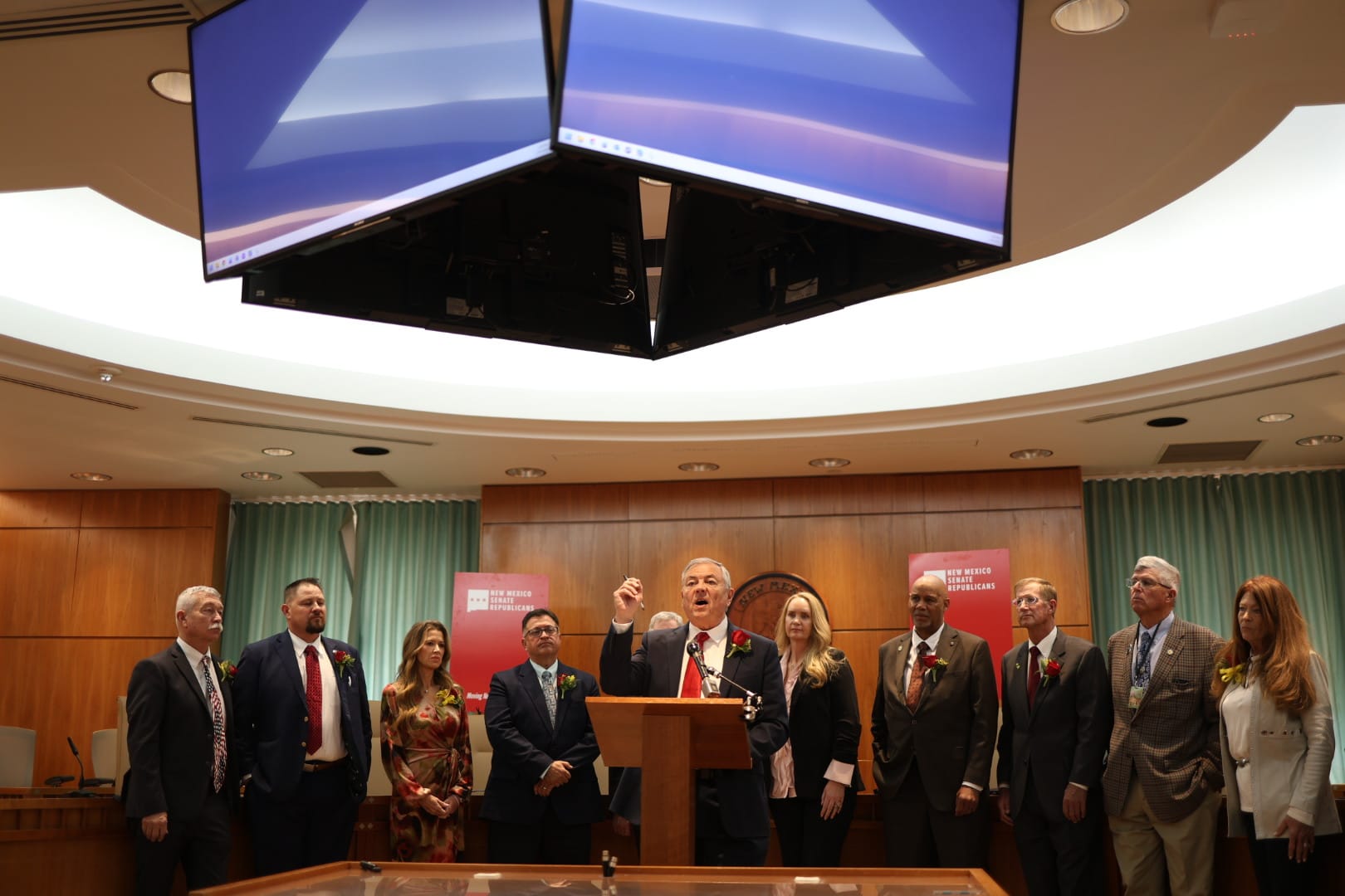 Sen. Bill Sharer speaks at a podium in the New Mexico Senate chamber as fellow Republican lawmakers stand behind him during a news conference.