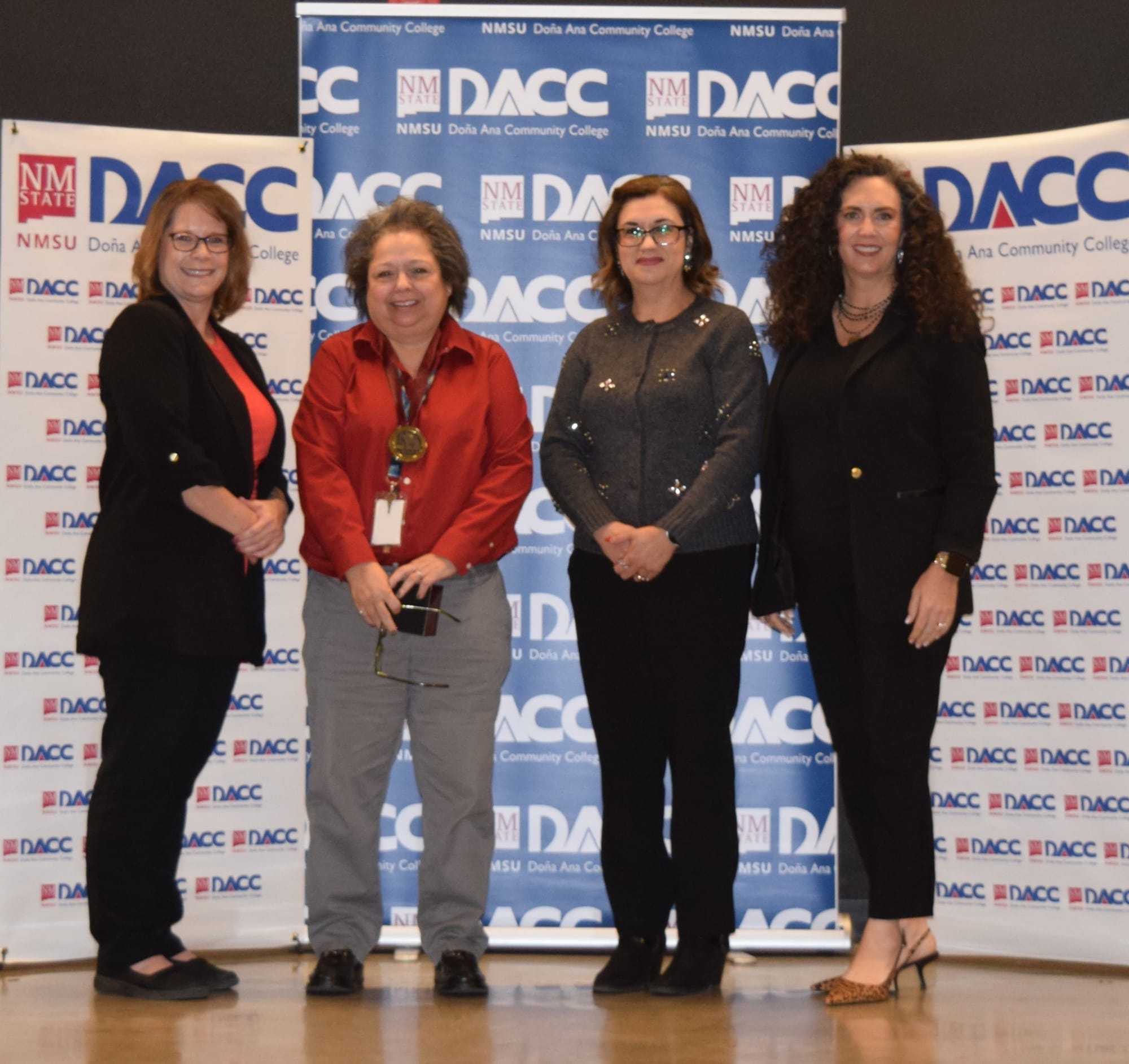 Mylis Murdock, Dr. Marnie Rocha, Michelle Guzman-Armijo and Shannon Bradley stand together in front of a DACC backdrop during a college event.
