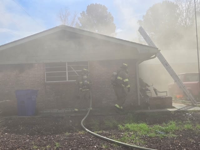 Firefighters work to extinguish a residential structure fire on Cedardale Drive in Las Cruces, with smoke filling the area as crews enter the home through the garage.