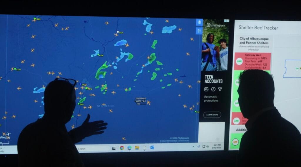 U.S. Rep. Gabe Vasquez and Bernalillo County Sheriff John Allen stand in silhouette before a large screen displaying a live map with aircraft and weather data during a Feb. 20, 2026 news conference in Albuquerque about drone use in local law enforcement.