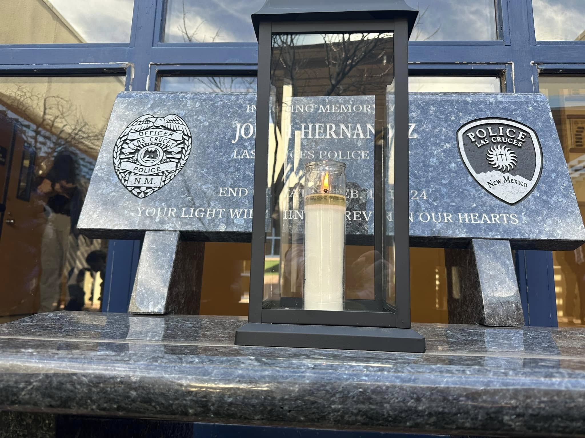 A memorial candle sits in front of a plaque honoring fallen Las Cruces police Officer Jonah Hernandez outside police headquarters.