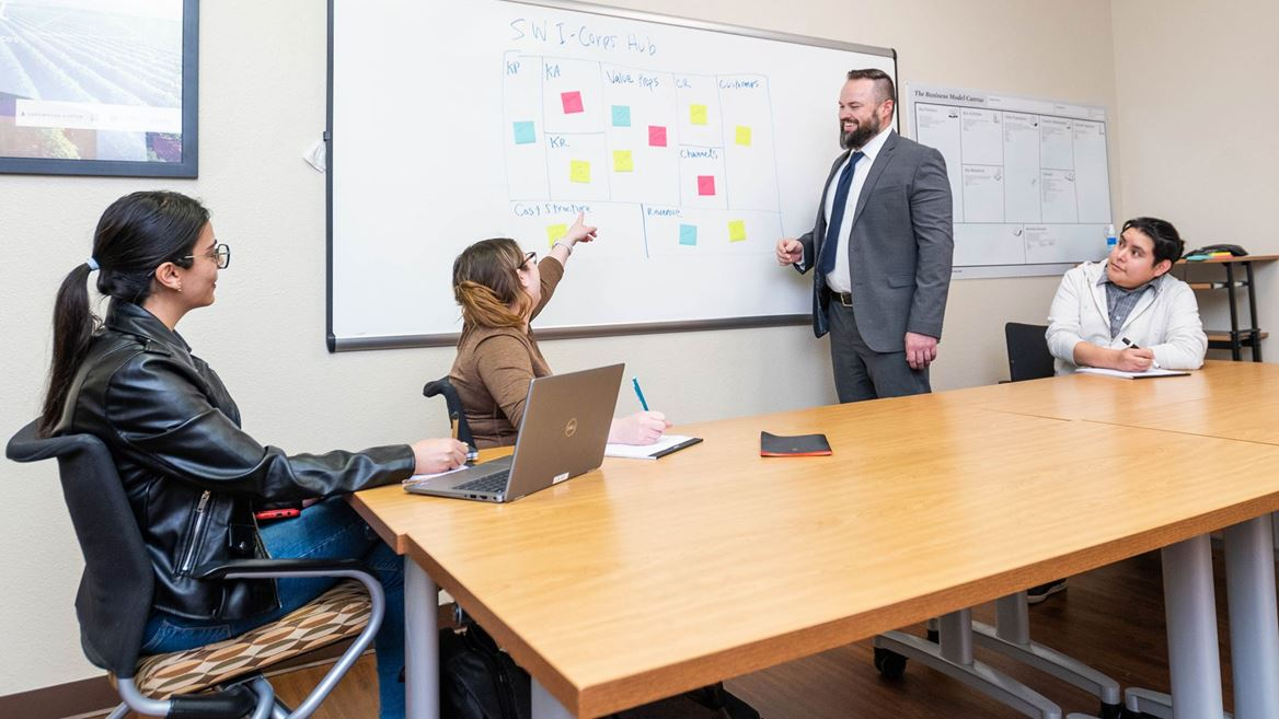 Small group meeting at NMSU’s Arrowhead Center with participants discussing ideas on a whiteboard during a business planning session