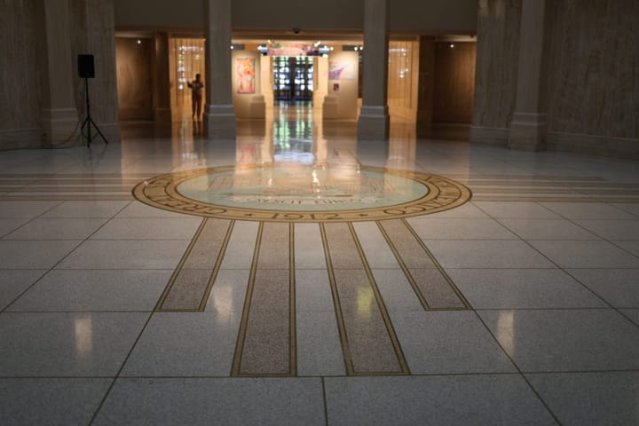 The New Mexico state seal is inlaid on the marble floor of the state Capitol in Santa Fe, with the Rotunda and art gallery visible in the background.