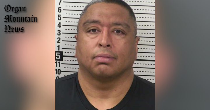 Former Las Cruces police officer Felipe Hernandez in a booking photo before a height chart, wearing a dark shirt.