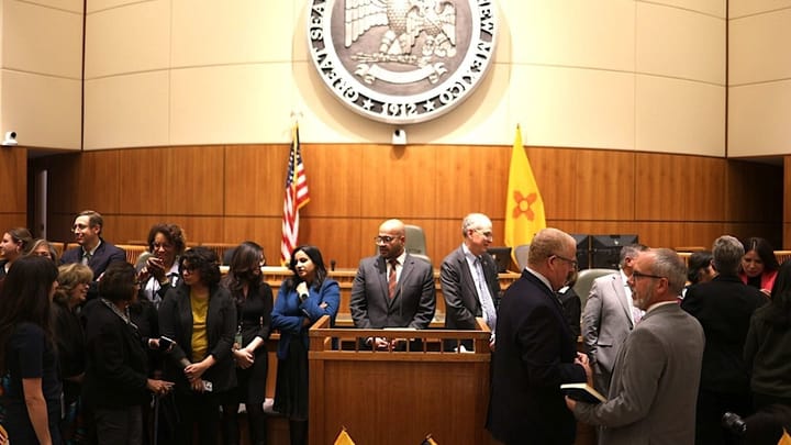 People gather and talk on the New Mexico House floor beneath the state seal and flags after the Nov. 10, 2025 special legislative session.