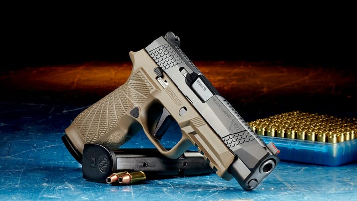 A tan and black semiautomatic handgun rests on a scratched blue surface next to a magazine, two loose bullets and a box of ammunition, with a dark background fading into warm orange light.