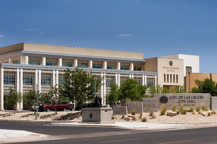 The exterior of Las Cruces City Hall, showing the main government building, landscaped grounds and City of Las Cruces signage along the street.