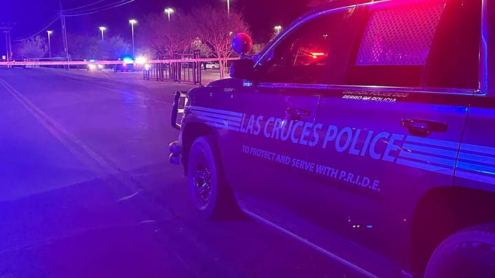 Las Cruces Police vehicle blocks a roadway at night as officers investigate a crash, with police tape stretched across the street and emergency lights illuminating the scene.
