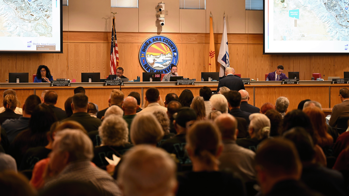 Residents fill the Doña Ana County Commission chambers as officials discuss Project Jupiter during a public meeting, with maps displayed on screens at the front of the room.