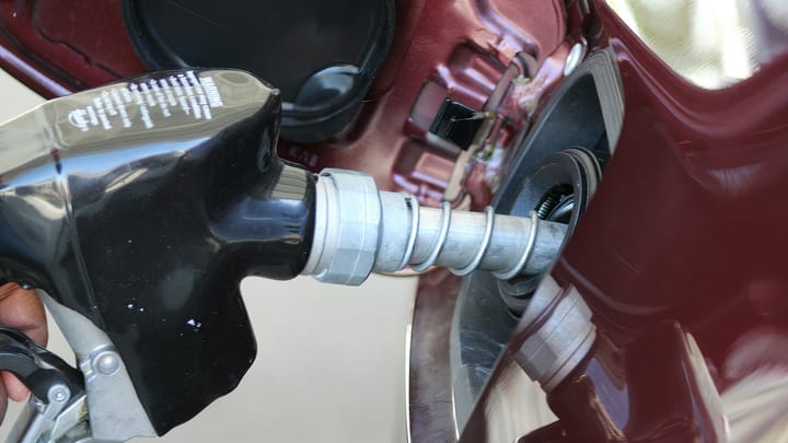 A gas pump nozzle inserted into a car’s fuel tank as gasoline is dispensed at a filling station.