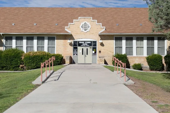 Front entrance of the Frank O’Brien Papen Center in Las Cruces, with a tan brick exterior, white trim, and a red-railed walkway leading up to double doors.