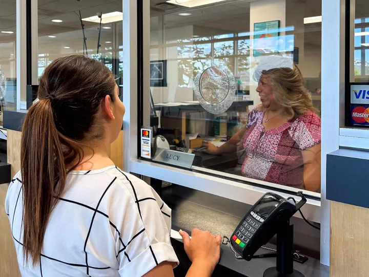 A customer stands at a cashier’s window inside Las Cruces City Hall while a staff member assists from behind the glass.