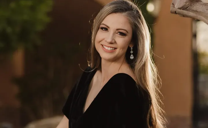Roxanne Livingston smiles while standing outdoors, wearing a black dress and drop earrings.