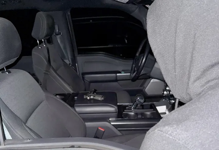 A hooded figure looks into a parked vehicle where a handgun is left on the center console.
