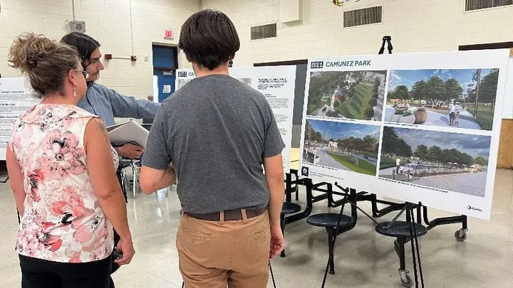 Three people review redevelopment renderings for Camuñez Park displayed on easels during a public meeting about the West Picacho and Motel Boulevard Metropolitan Redevelopment Area plan.