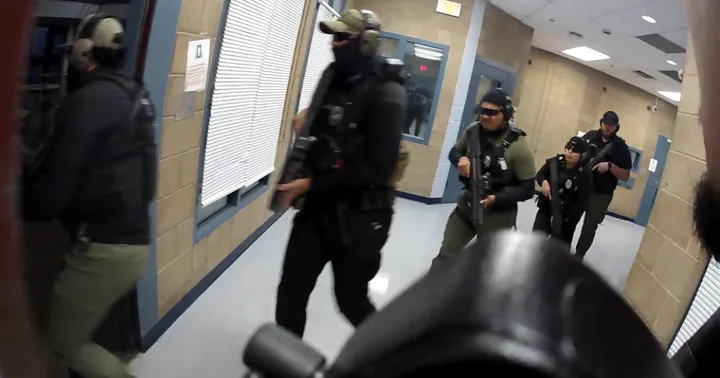Armed detention officers in tactical gear move in formation down a hallway inside the Doña Ana County Detention Center during a training or raid scenario.