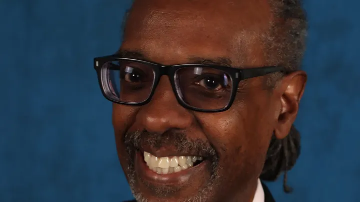 Close-up portrait of Gene Grant smiling against a blue background.