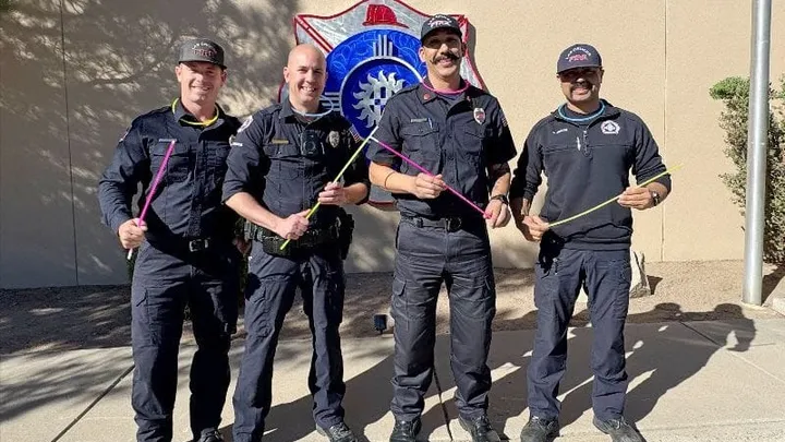 Four Las Cruces firefighters smile while holding colorful glow necklaces outside a city fire station ahead of Halloween.