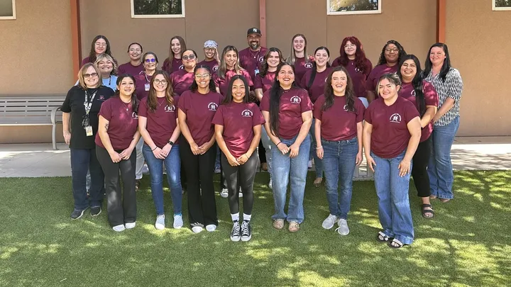 Group photo of NMSU social work students and Las Cruces Public Schools staff standing outside, many wearing matching maroon shirts.