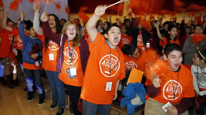Sixth-grade students wearing orange “Future Aggies” shirts cheer and wave pom-poms during a past Young Achievers Forum event at New Mexico State University.