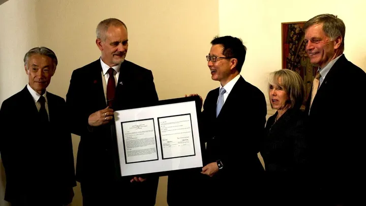 Five people stand together holding a framed document during a signing ceremony marking a new partnership between New Mexico State University and a Japanese technology company.