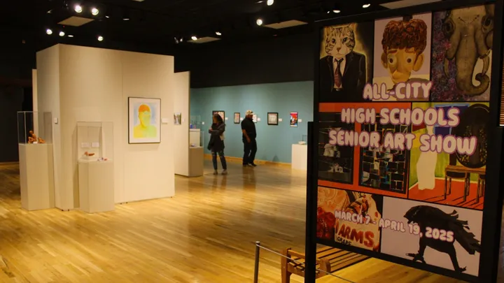 Gallery view of the Branigan Cultural Center’s All-City High School Senior Art Show, featuring student artwork on display and a colorful sign promoting the 2025 exhibition.