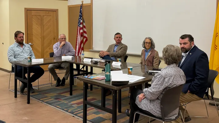 Panelists sit around a conference table during a roundtable discussion on public lands and health care impacts in Albuquerque, with U.S. and New Mexico flags visible behind them.