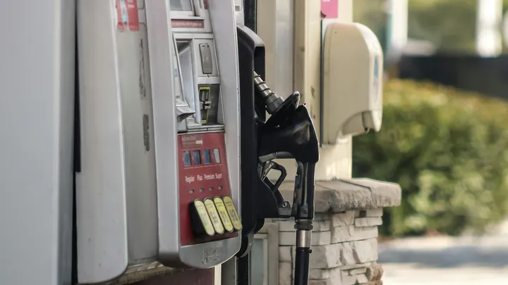 Close-up of a gas pump with a black fuel nozzle resting in its holder beside grade selection buttons at a service station.