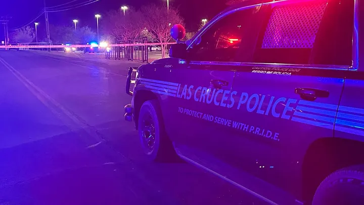 Las Cruces Police vehicle blocks a roadway at night as officers investigate a crash, with police tape stretched across the street and emergency lights illuminating the scene.