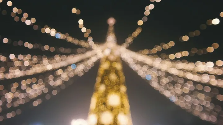 A blurred view of a Christmas tree and strands of holiday lights glowing against the night sky.