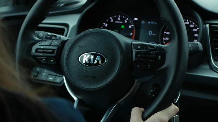 Driver’s view of a Kia vehicle interior, with hands on the steering wheel and the Kia logo visible at the center of the wheel.