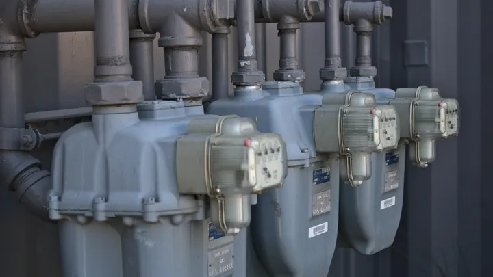 A row of natural gas meters mounted on an exterior wall, showing gauges and piping used to measure residential heating usage.