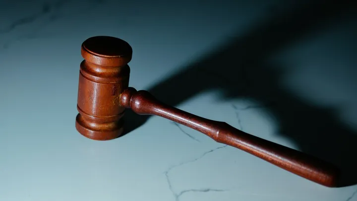 A wooden judge’s gavel rests on a light-colored surface, casting a shadow under directional lighting.