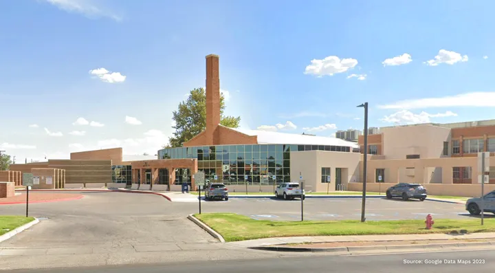 Exterior view of the Third Judicial District Court building in Las Cruces, New Mexico, with glass facade, brick chimney and front parking area visible under a clear sky.