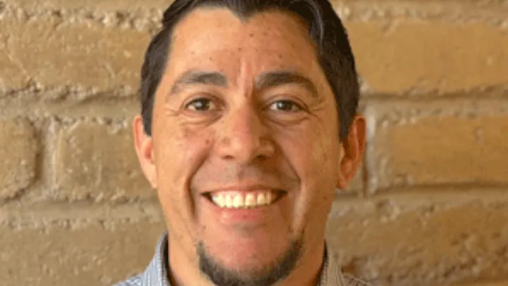 Mesilla Mayor Russell Hernandez smiles in a headshot portrait against a brick wall background.