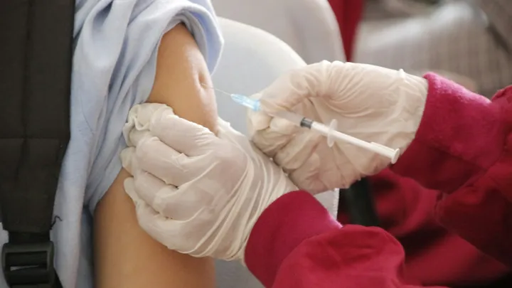 A health care worker administers a vaccine injection into a patient’s upper arm.
